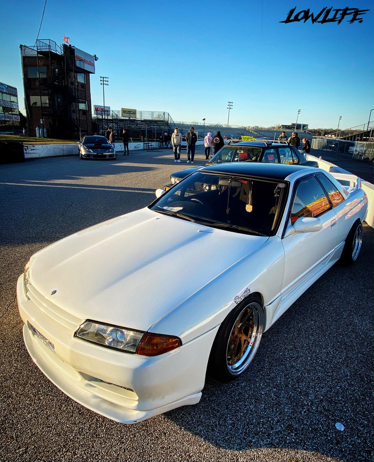 Lowlife community gathering with modified cars at a raceway