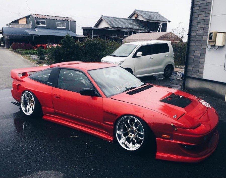 Red modified Nissan 180SX parked on a wet street